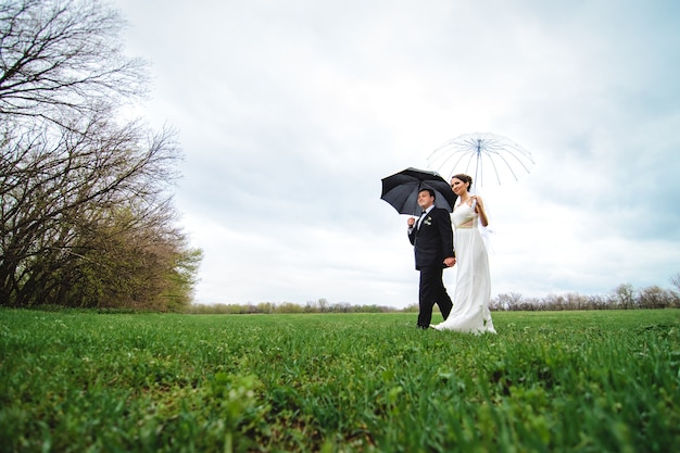 傘の下を歩く雨の結婚式の日の新郎新婦