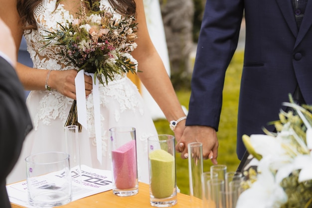 Photo bride and groom next to the sand of different colors in the glass vase at the marriage unity ceremony sand ceremony