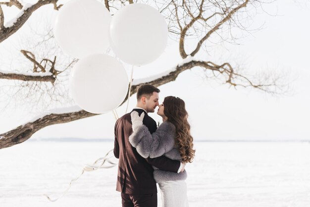 Жених и невеста среди снежного пейзажа с большими белыми воздушными шарами