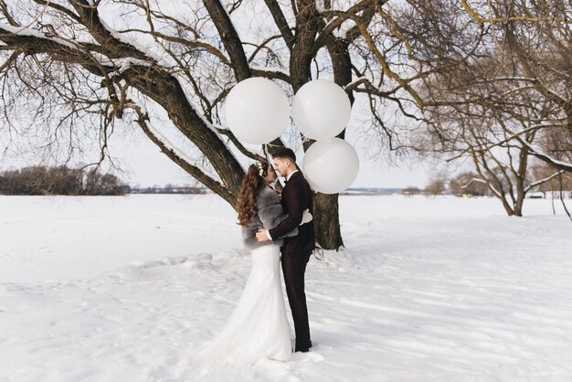 Bride and groom among snowy landscape with big white balloons