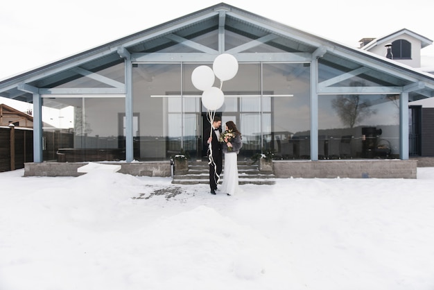 Bride and groom among snowy landscape with white big balloons