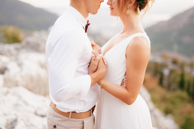 The bride and groom stand embracing among the mountains holding hands and look at each other closeup