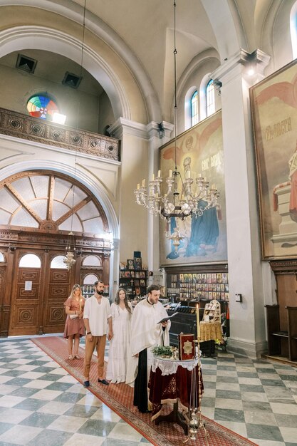 Bride and groom stand in front of a priest conducting a wedding ceremony in a church with a bible at