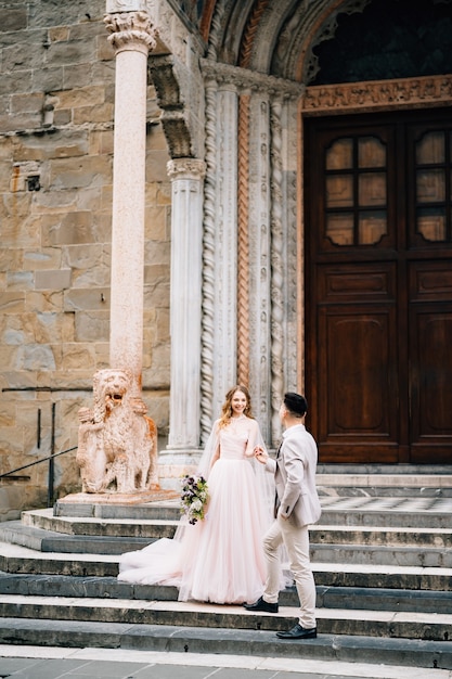 Bride and groom stand holding hands on the steps at the entrance to the basilica of santa maria