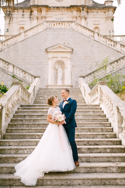 The bride and groom stand hugging on the stairs of the nativity of the blessed virgin mary church in