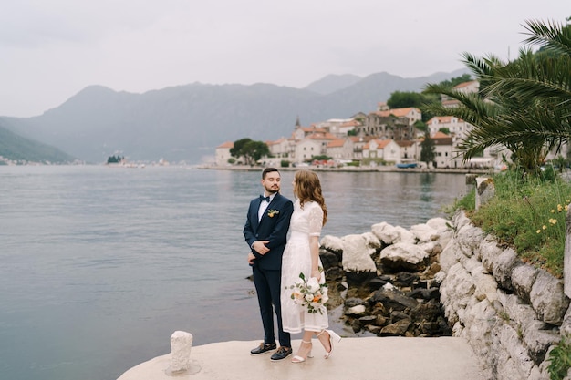 Bride and groom stand on the pier by the water against the background of perast montenegro