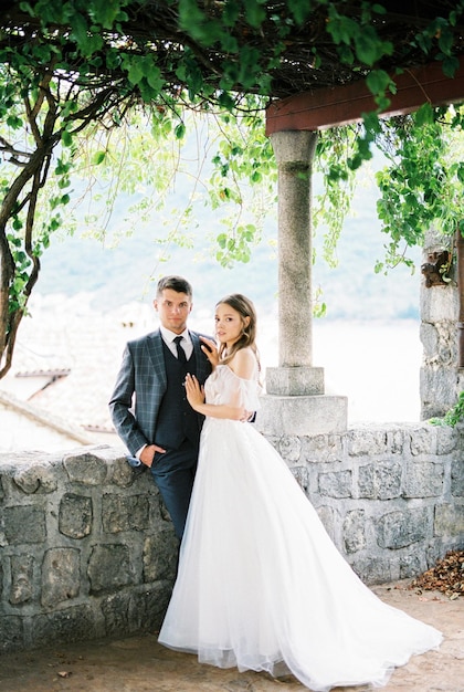 Bride and groom stand in a stone gazebo covered with ivy