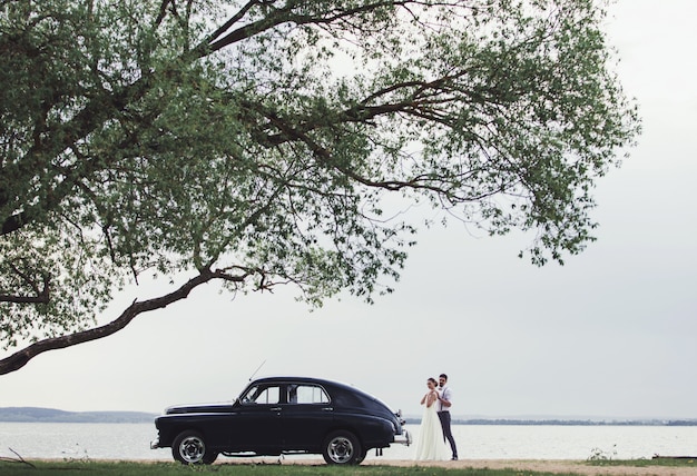 Bride and groom standing near a retro car