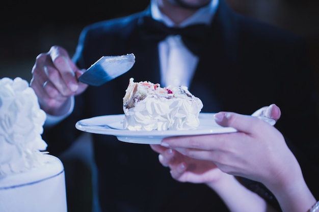 Bride and groom tasting luxury wedding cake decorated with roses at reception, catering in restaurant