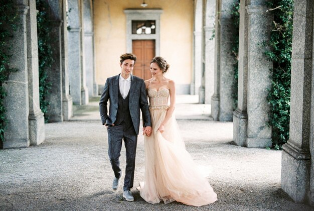 Bride and groom walk holding hands along the terrace of an old villa