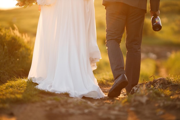 A bride and groom walk together on a trail at sunset.