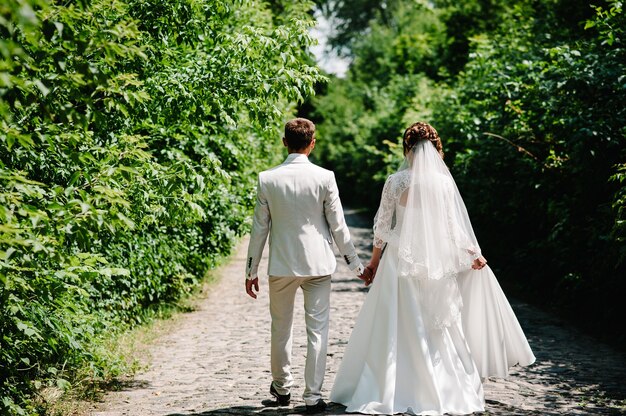 Bride, groom walking on way spring forest.