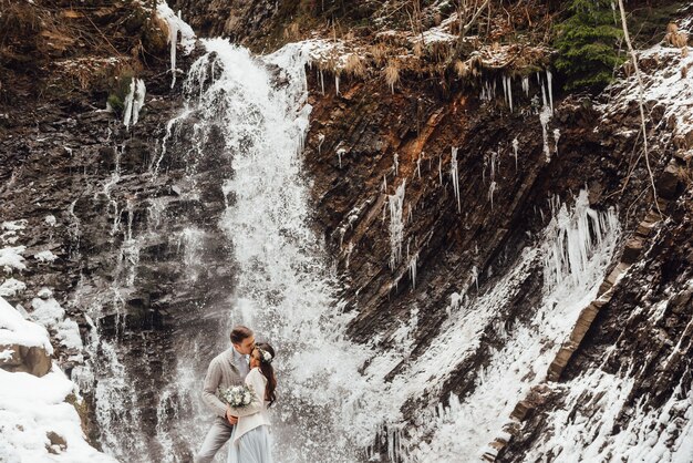 Photo bride and groom on the wall of a mountain waterfall