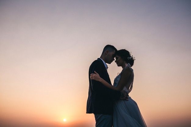 Bride and groom watch the sunset standing on the hill