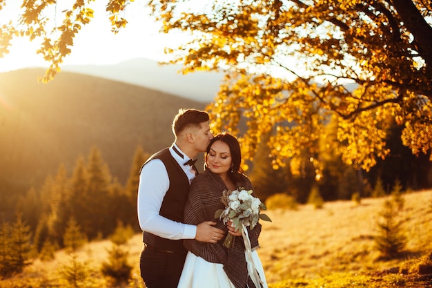 Bride and groom watch the sunset standing on the hill