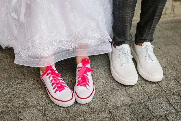 The bride and groom wearing pink sneakers Concept funny wedding couple The newlywed together Textile sneakers flat shoes Close up Top view View of the bottom of the feet and shoes