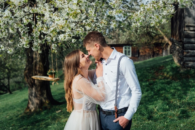 春の自然の中で屋外を歩く結婚式の日の花嫁と花婿。ブライダルカップル、緑豊かな公園で抱きしめる幸せな新婚の女性と男性。屋外の愛情のある結婚式のカップル。