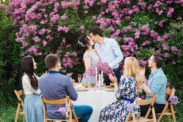 Foto sposi a un tavolo di nozze con gli amici in un giardino primaverile