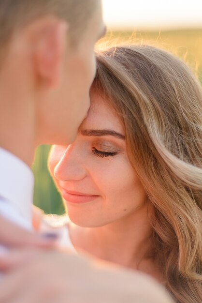 Foto sposa e sposo in un campo di grano. un uomo bacia un amato sulla fronte.