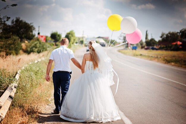 Bride and groom with balloons walking together on the road