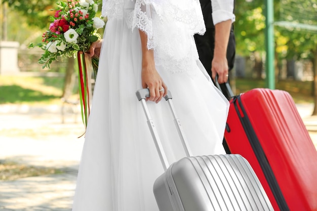 Bride and groom with big suitcases walking outdoors closeup