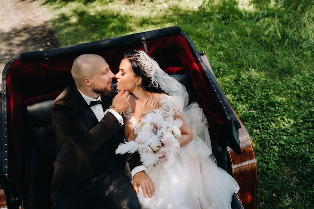 Foto gli sposi con un bouquet sono seduti in una carrozza nella natura in stile retrò