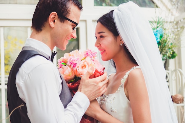 Photo bride and groom with flower bouquet against window