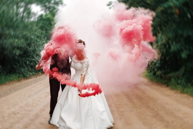 Bride and groom with the red colored smoke in the summer park