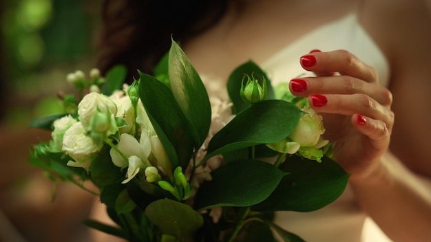 Bride hands hands holding bouquet in park Unknown girl touching roses outdoors in slow motion Unrecognizable woman standing with white roses in garden