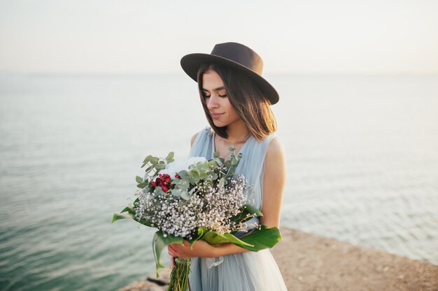 Sposa in cappello e abito da sposa blu che tiene il mazzo di fiori