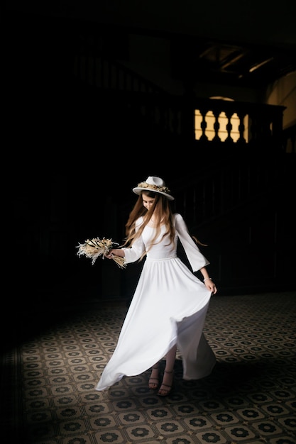 The bride in a hat and a bouquet Portrait of a bride in a white dress Portrait of the bride Young girl in a white wedding dress and hat with a bouquet of flowers