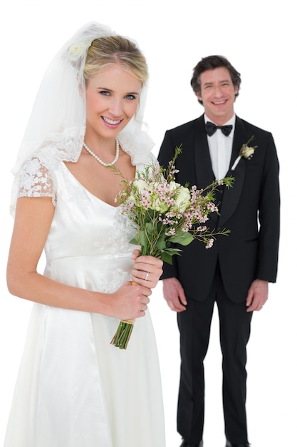 Bride holding bouquet with groom in background 