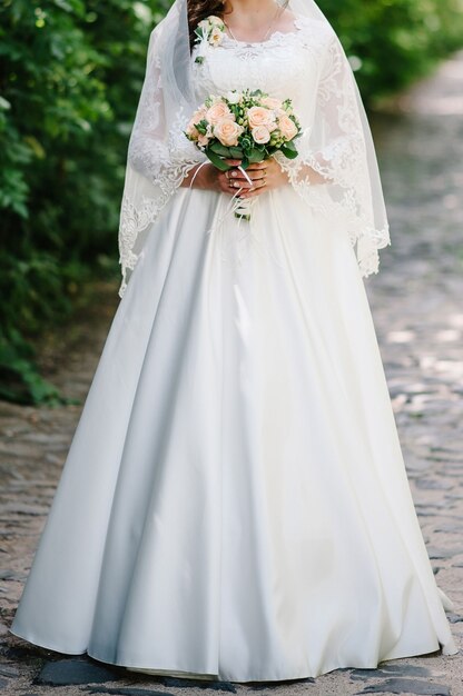 Bride holding hand bouquet of pastel pink flowers and greens with ribbon at nature.