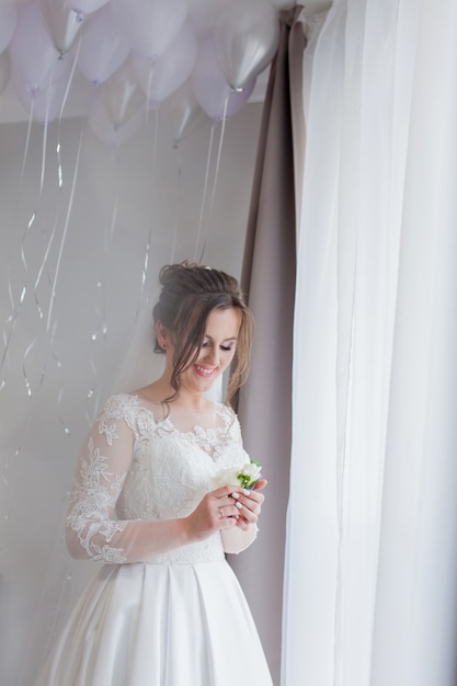 The bride holding in hand close-up the groom's buttonhole flowers with white roses, and green and greenery. Bride's Preparations. Wedding Morning concept.