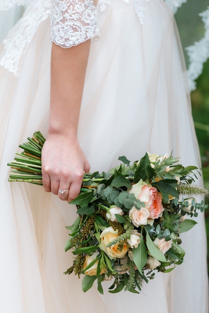 Bride holding in her hands delicate, expensive, trendy wedding bouquet of greenery and roses.Classic bridal flowers in orange and pink colors