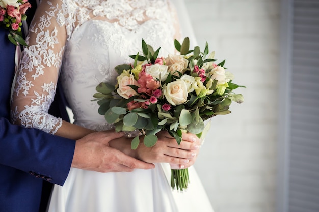 Sposa che tiene un mazzo di nozze nelle mani che stanno sposo vicino