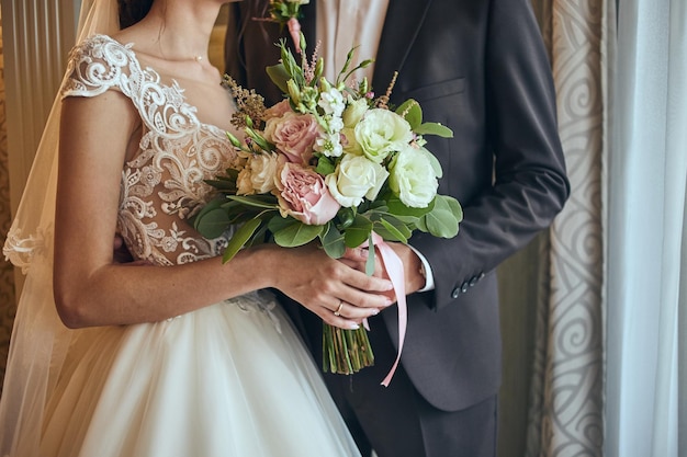 Sposa che tiene un mazzo di nozze nelle mani che stanno sposo vicino