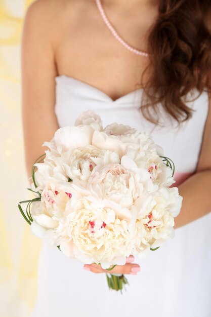 Sposa azienda bouquet da sposa di peonie bianche alzato su sfondo chiaro