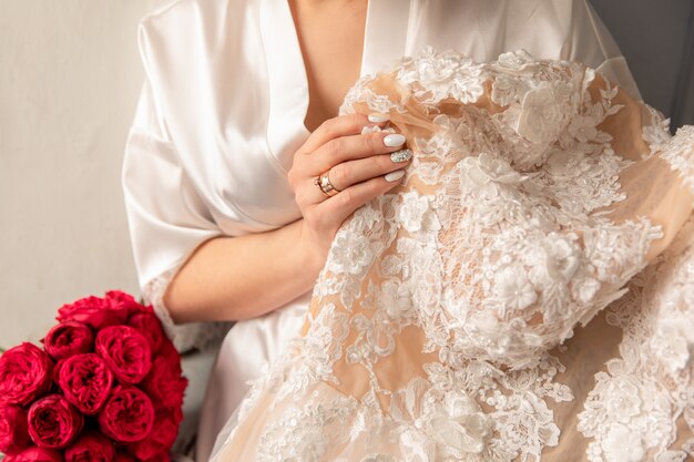 Bride holding white wedding dress with lace, embroidery.