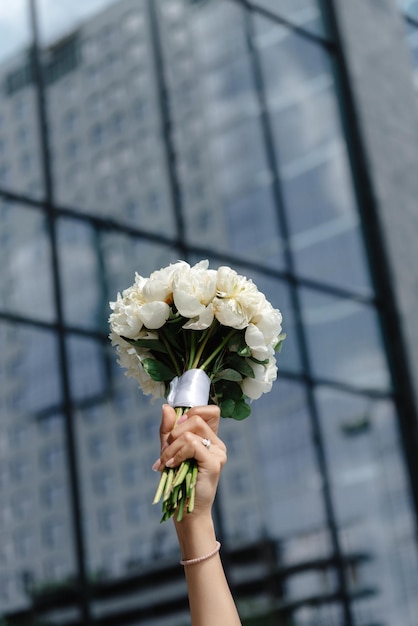 The bride holds the bouquet high above her head in front of the building