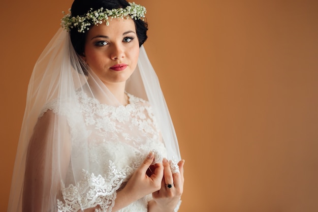 The bride holds bridal veil in her hands and look at camera