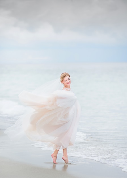 Bride holds her dress up standing in the sea water on the beach