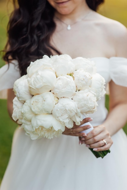 The bride holds in her hands a wedding bouquet of white peonies