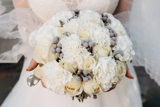 The bride holds a large luxury wedding bouquet of white roseson the front of the dress