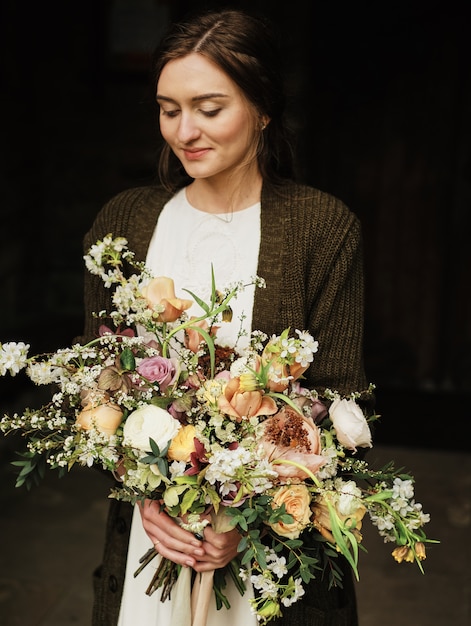 Photo bride holds wedding bouquet and looks down over cloudy day. close-up, big beautiful bouquet