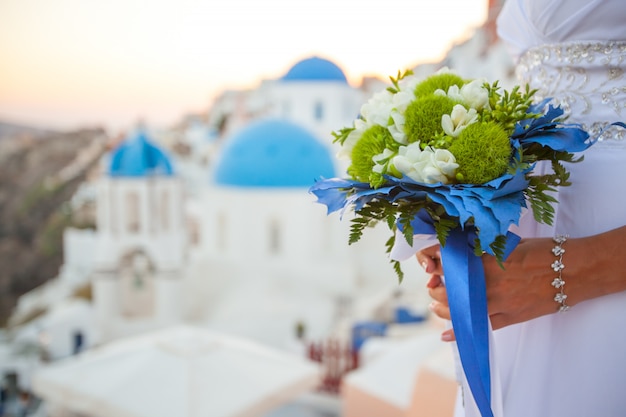 Photo bride holds wedding bouquet in white and green colors and blue decor. the sunset over santorini, greece