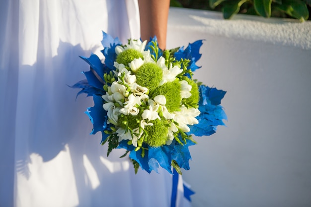 Bride holds wedding bouquet in white and green colors and blue decor.