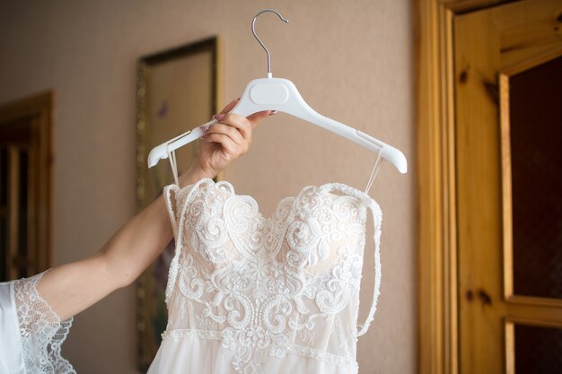 The bride holds the wedding dress on a hanger