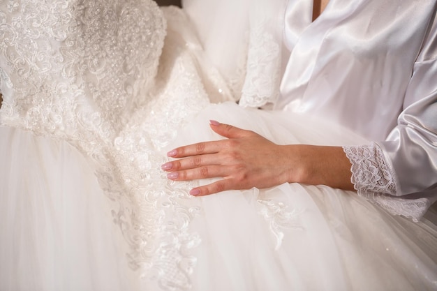 The bride holds a white dress in her hands on the wedding day.