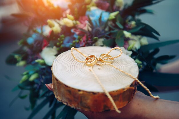 Bride holds wooden stand with golden wedding rings, rings on wooden stand